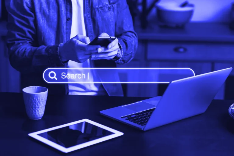 Person searching on a phone next to a laptop and tablet