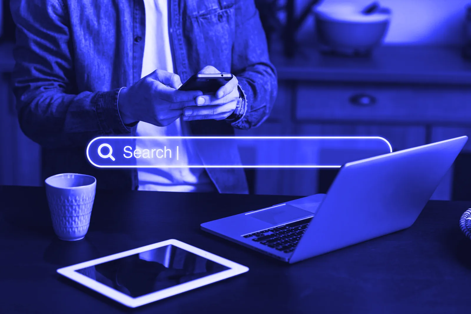 Person searching on a phone next to a laptop and tablet